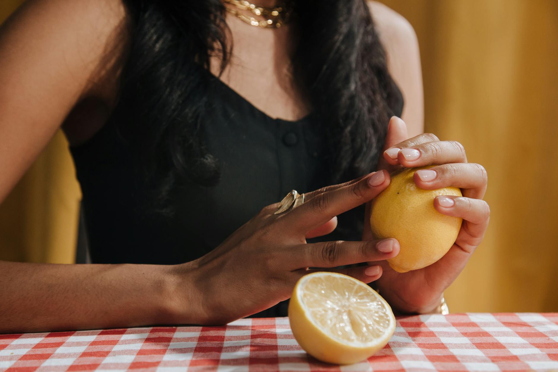 A hand holding a fresh lemon on a soft pink background, symbolizing the gentle approach to clitoral pleasure.