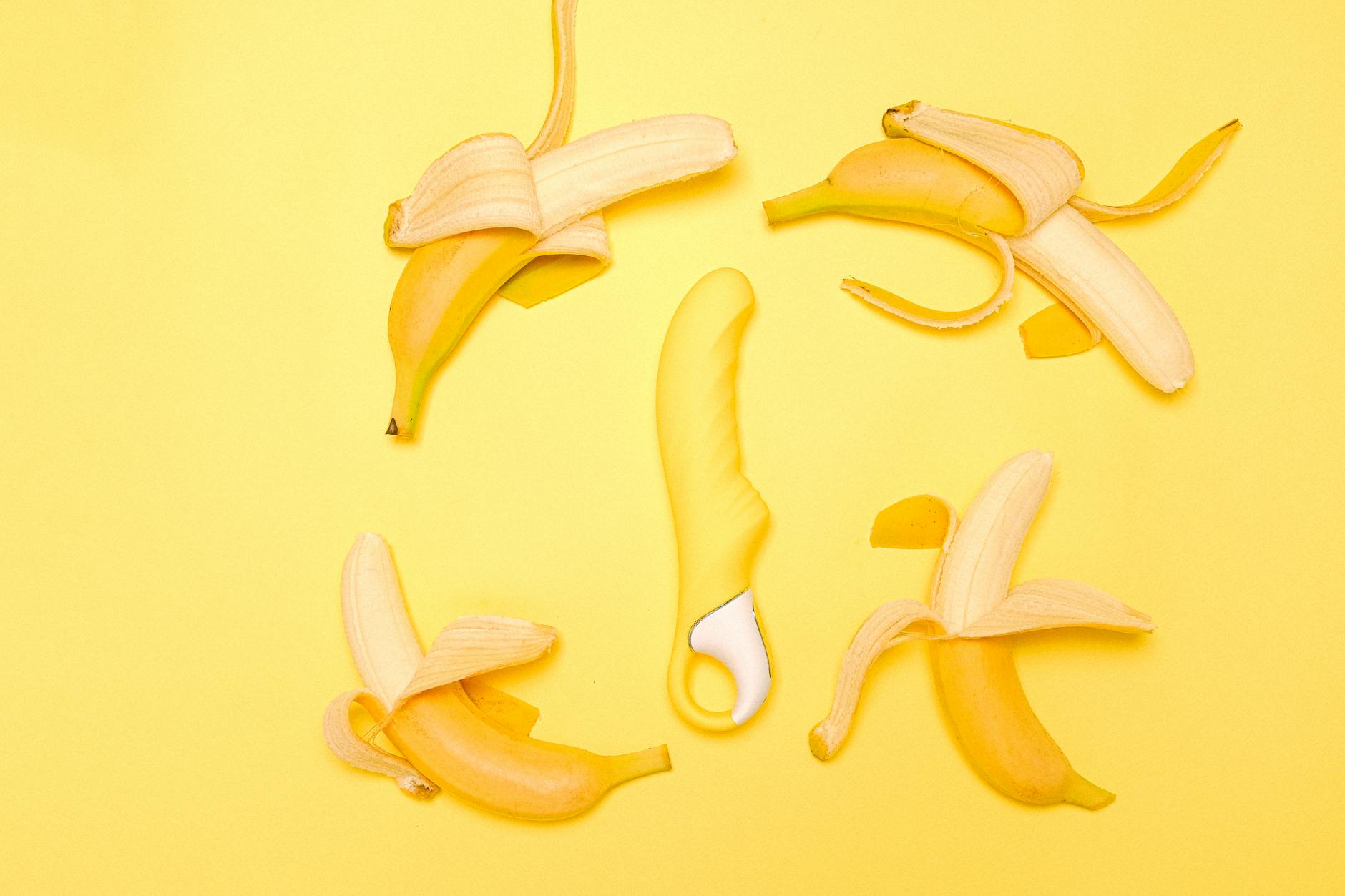 Yellow lemon clitoral vibrator with peeled bananas on bright yellow background