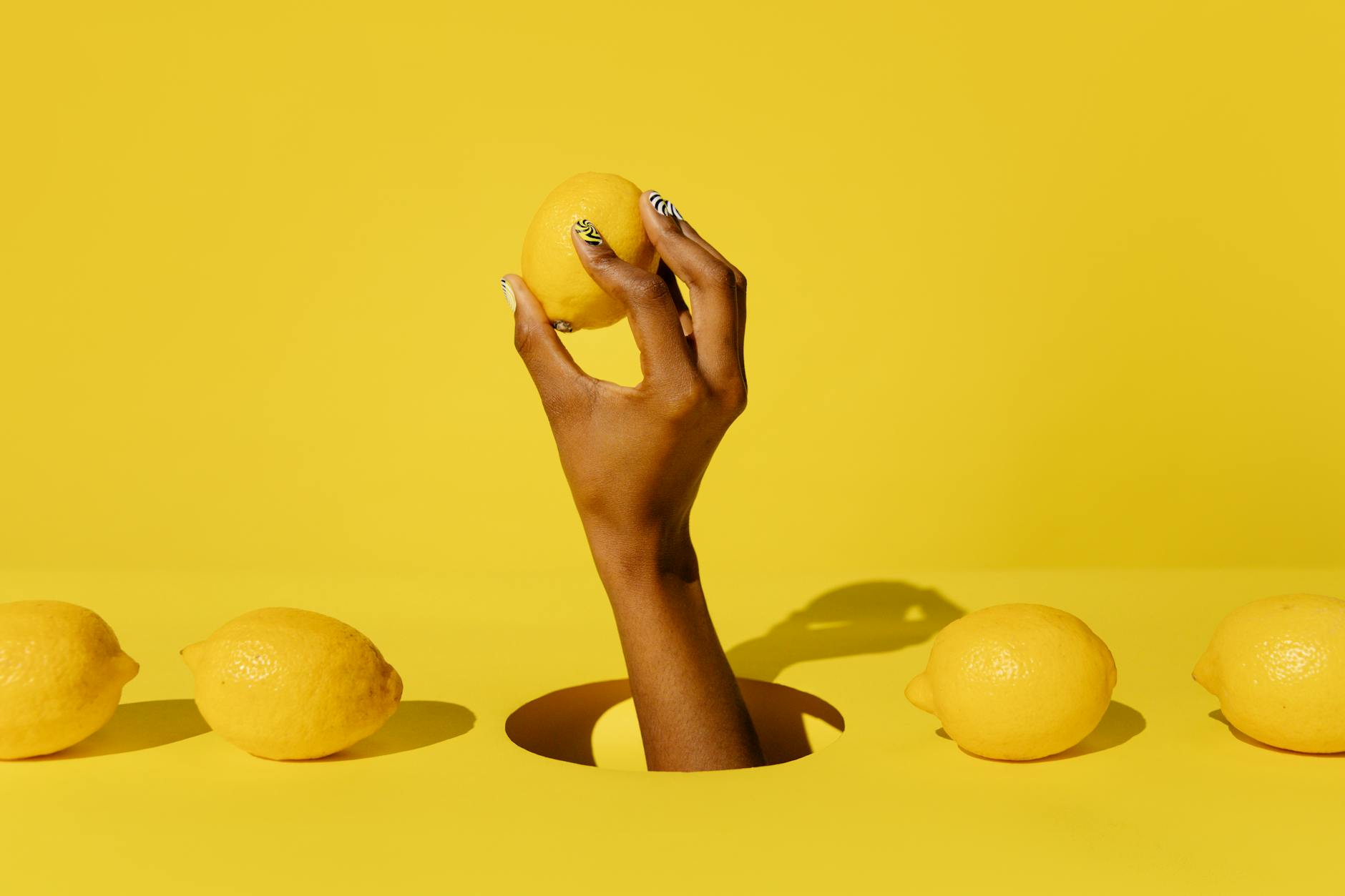 Hand holding a fresh lemon against a vibrant yellow background, symbolizing the citrusy simplicity of external-only pleasure
