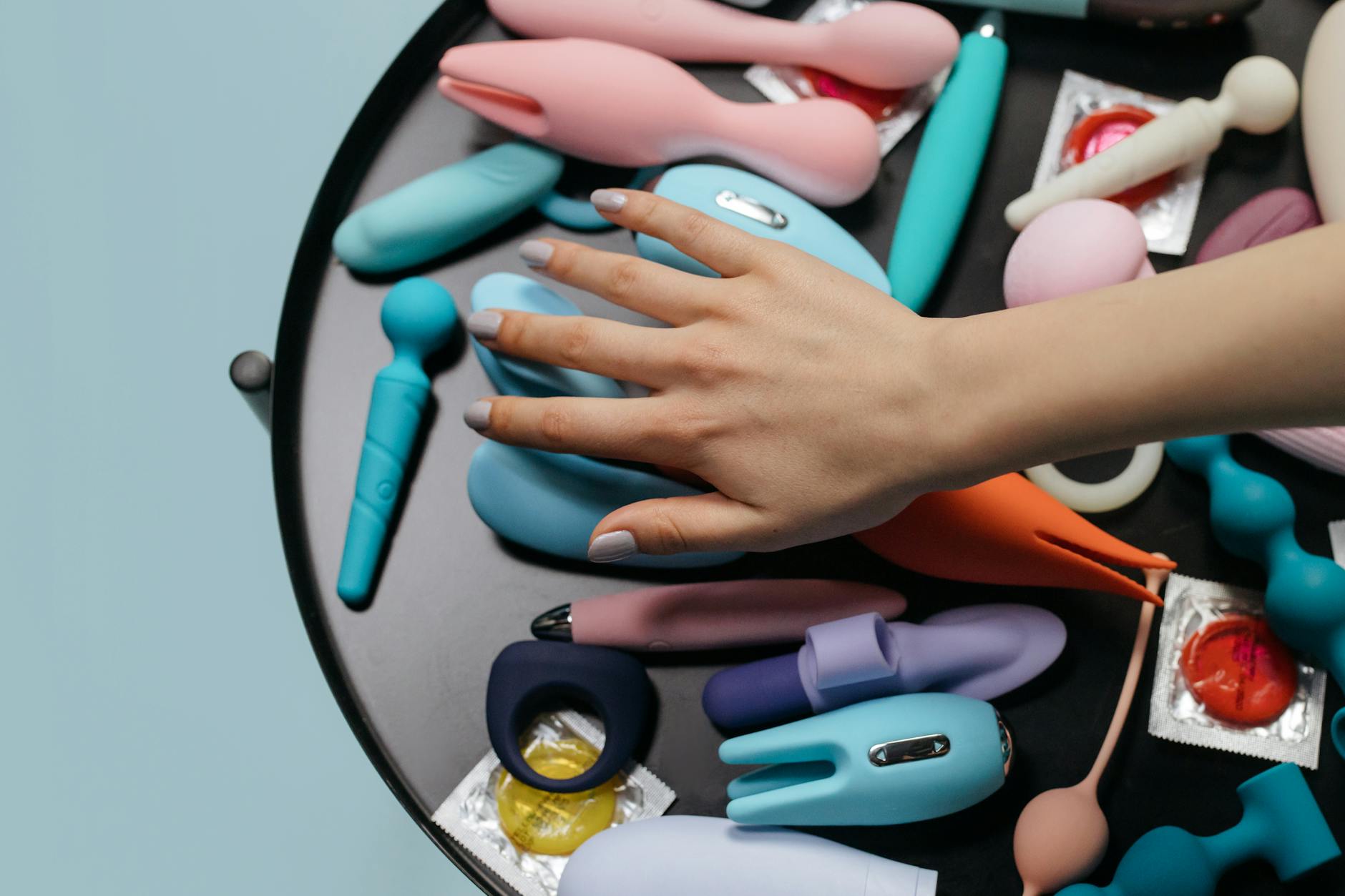 A hand reaching over a variety of colorful vibrators arranged on a table.
