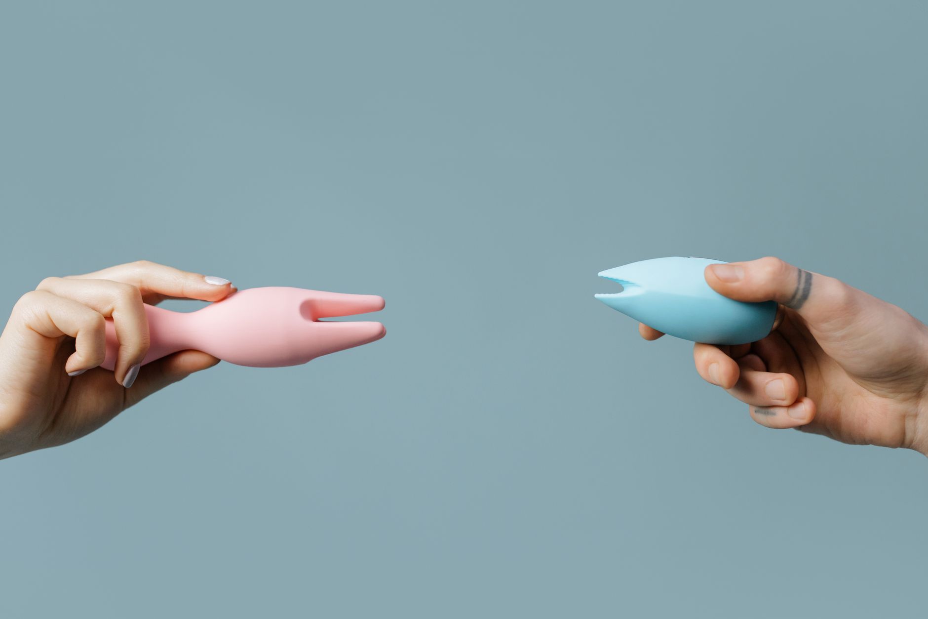 Woman holding two colorful clitoral vibrators against purple background.