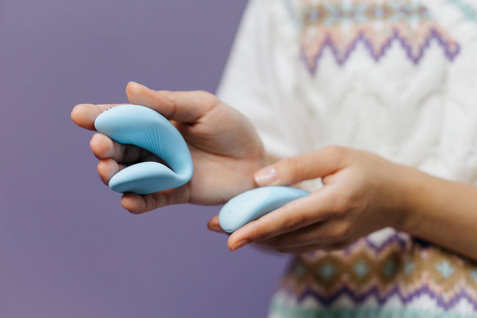 Hand holding a sleek blue air-suction vibrator against a purple background