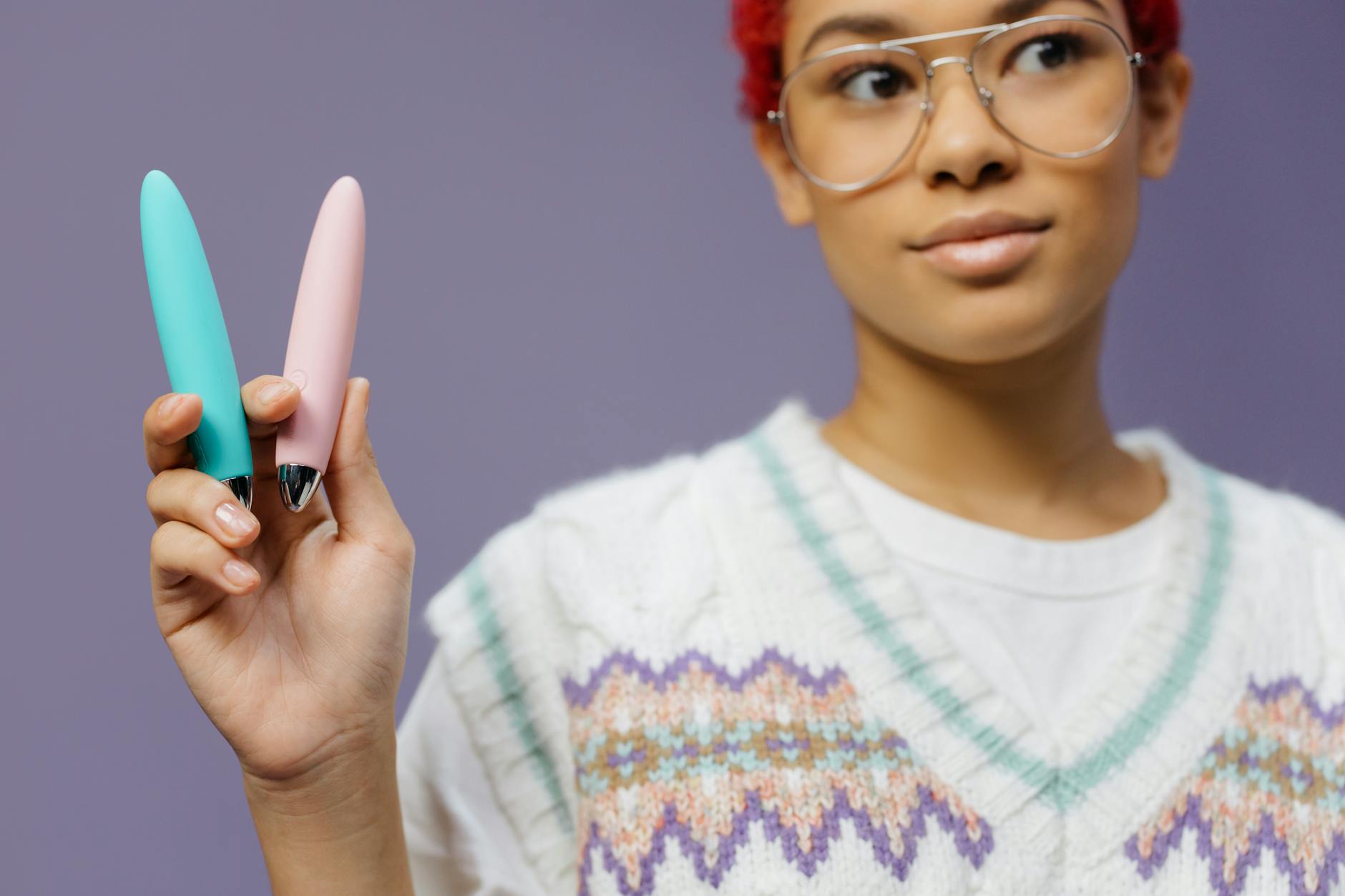 Une jeune femme tenant deux vibrateurs colorés contre un fond violet