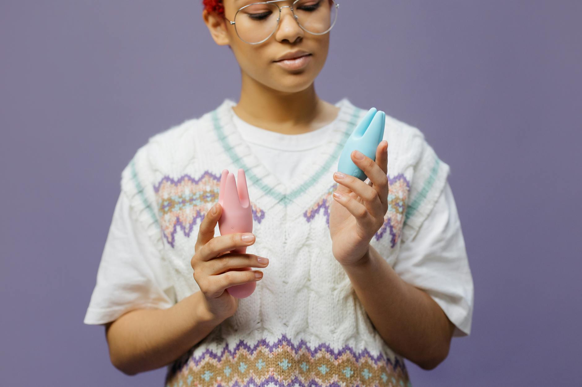Person in glasses holding blue and pink silicone vibrators with intention and care.