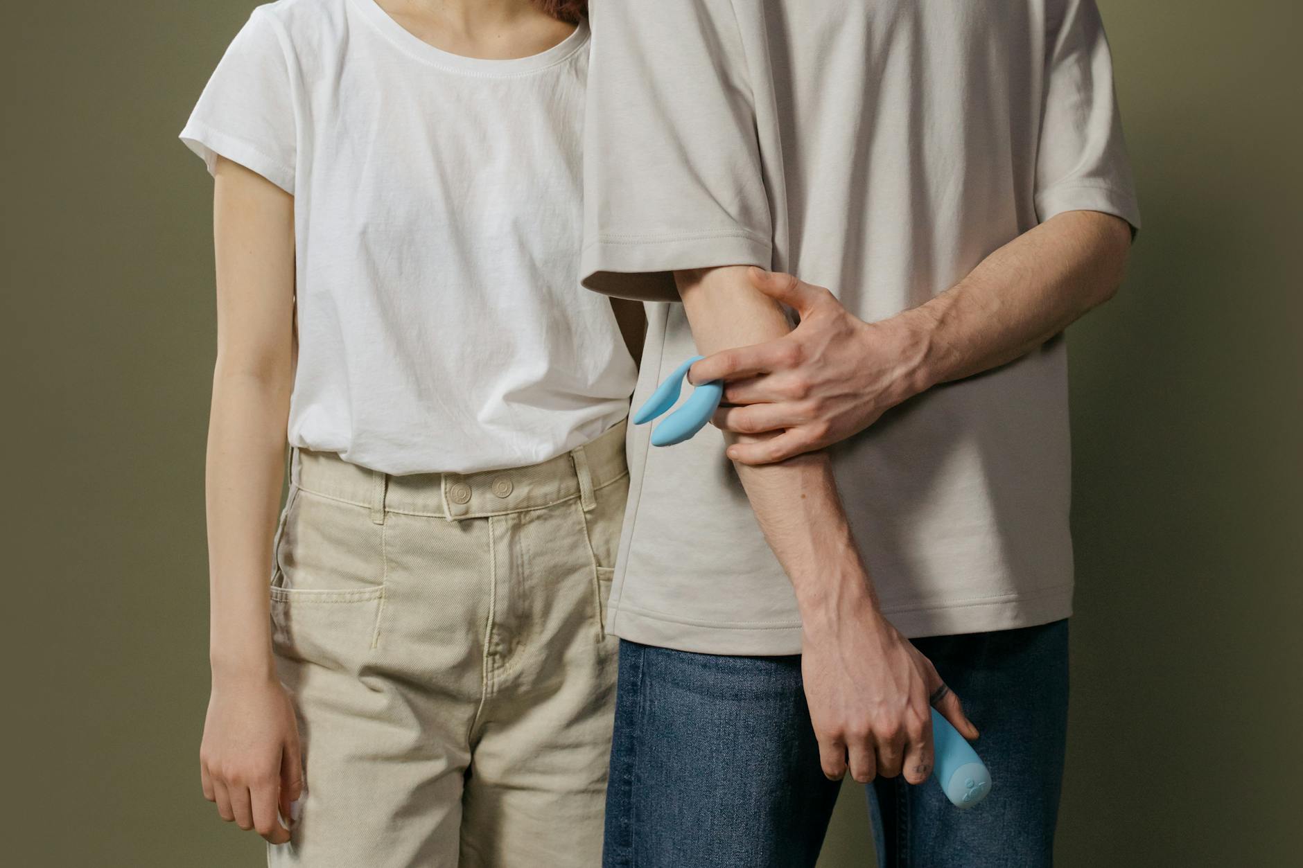 A couple standing close together holding a blue vibrator, representing modern approaches to shared intimacy and pleasure.